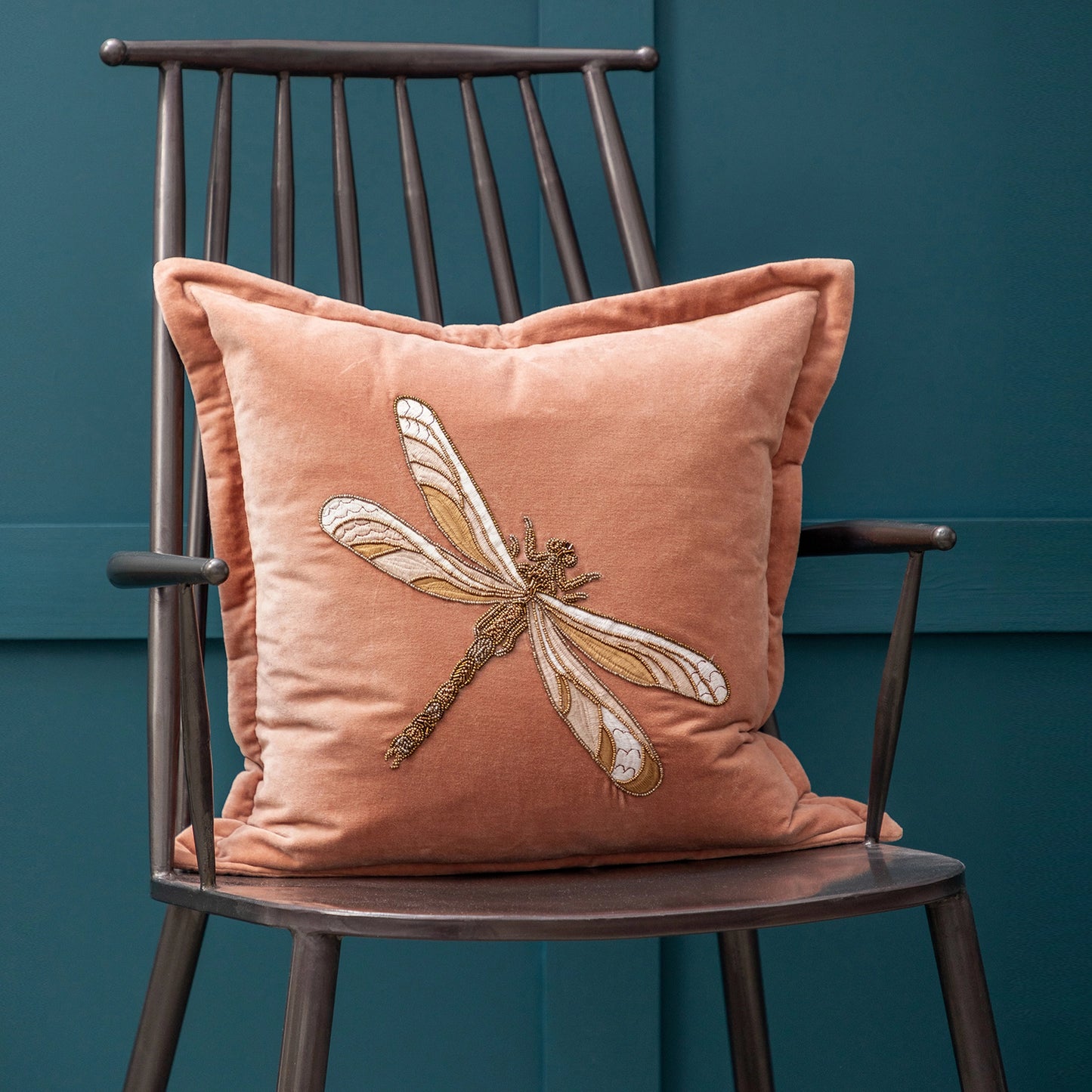 Pink pillow with dragonfly design on a wooden chair against a teal wall