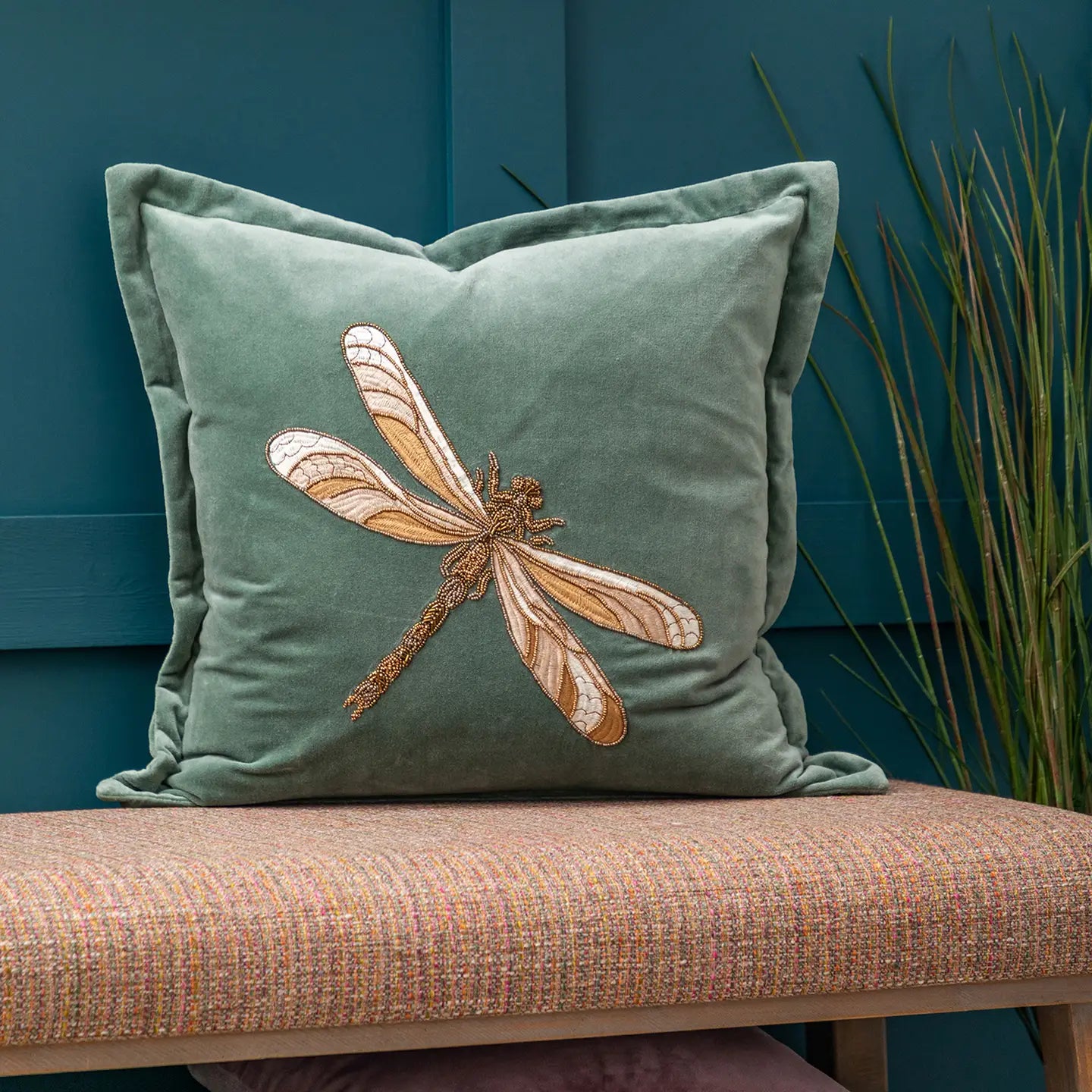 Teal pillow with dragonfly design on a bench against a blue wall