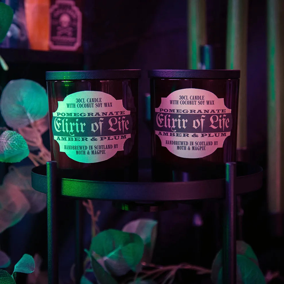 Two candles labeled 'Ellixir of Life' on a stand with a colorful background.