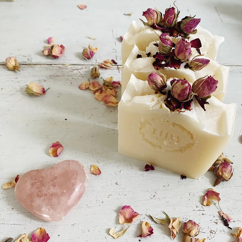 Two bars of Love Handmade Luxury Soap with dried flowers on a rustic wooden surface