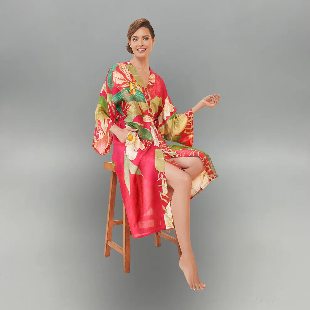 Woman wearing a colorful floral kimono sitting on a wooden stool against a gray background