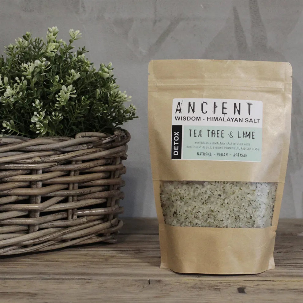 Bag of 'Ancient Wisdom Himalayan Batch Salt - Detox Blend' with tea tree & lime on a wooden surface next to a basket with greenery.