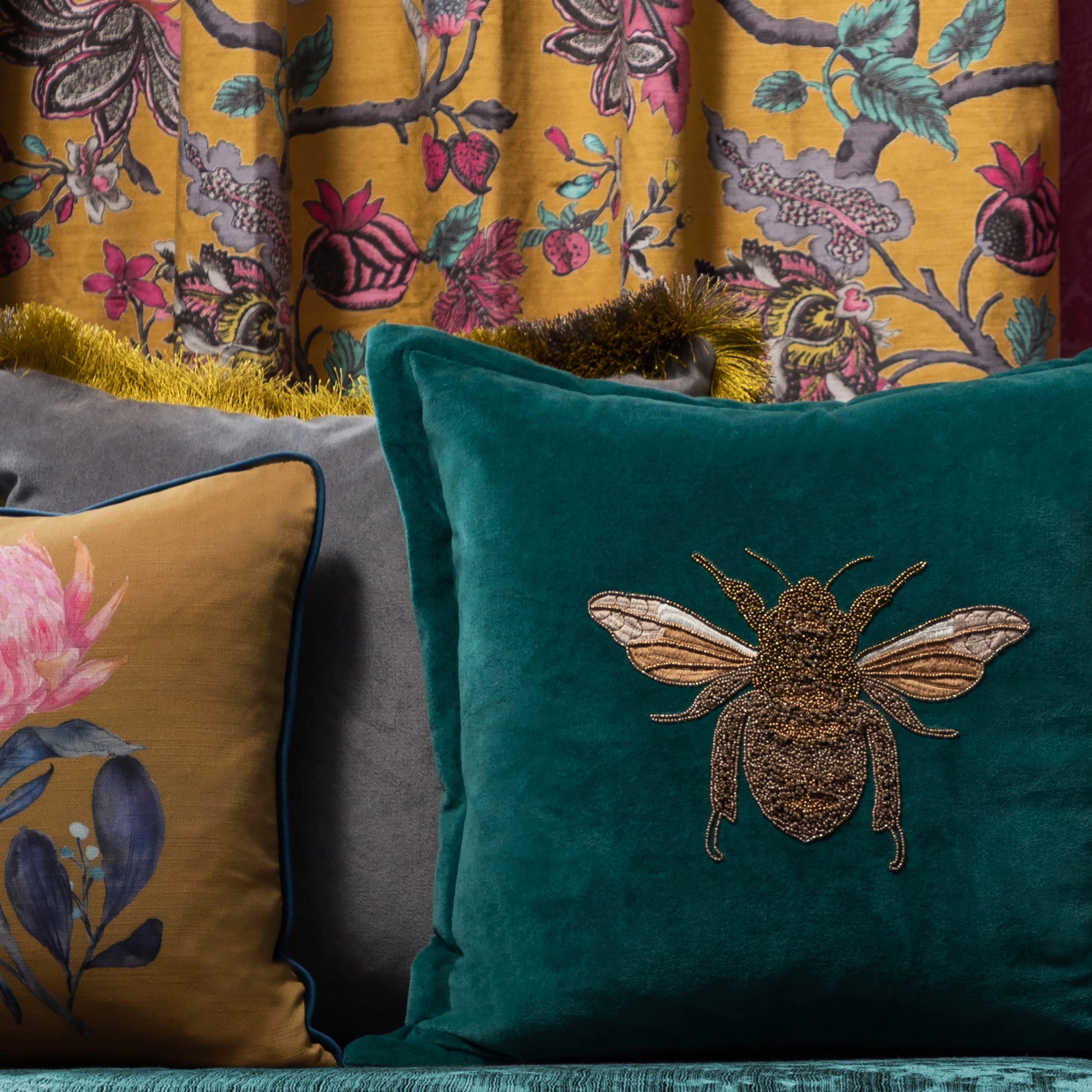 Teal pillow with a gold embroidered bee design on bench
