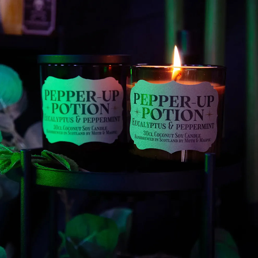 Candle labeled 'Pepper-Up Potion' with a green glow in a dark setting