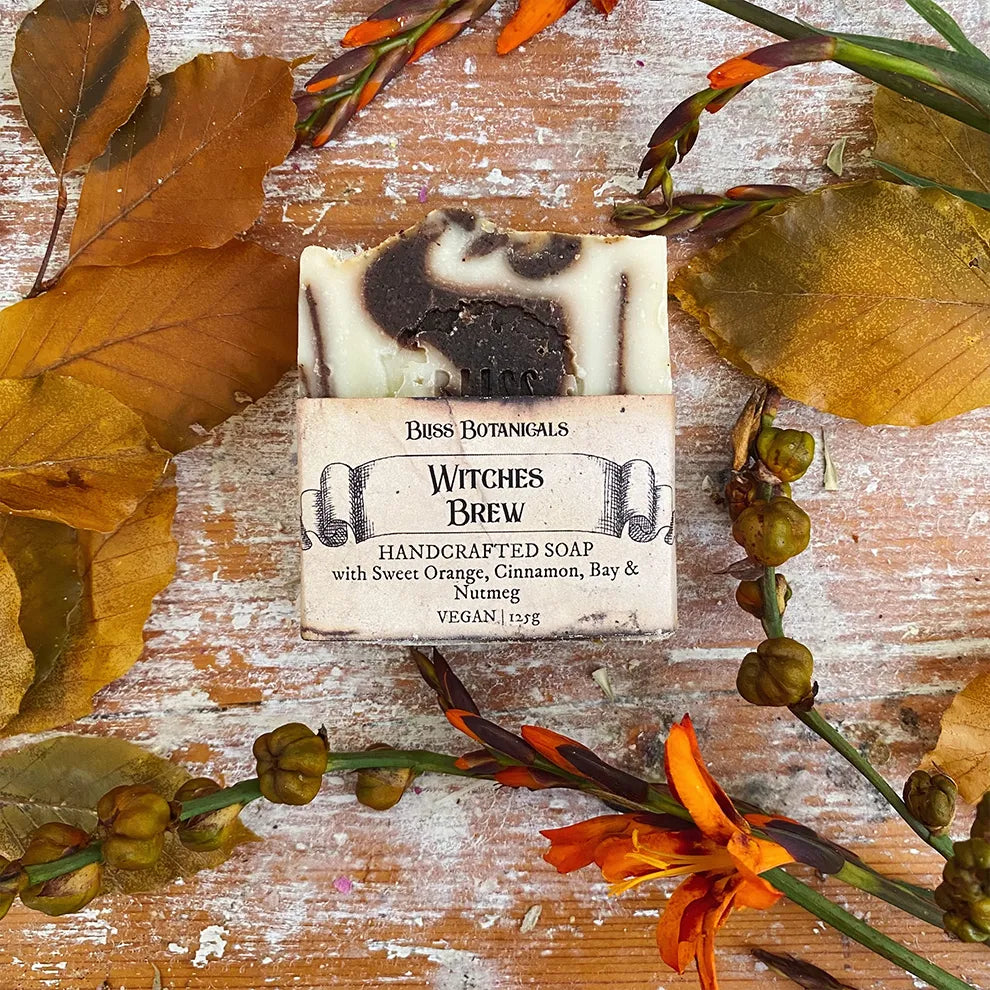 Bar of Witches Brew luxury soap surrounded by autumn leaves and flowers on a wooden surface.